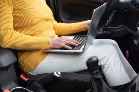 Businesswoman sitting in car and using her laptop