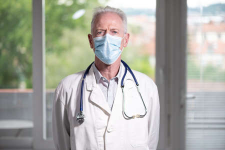 Portrait of senior doctor with arms crossed wearing a face maskの写真素材