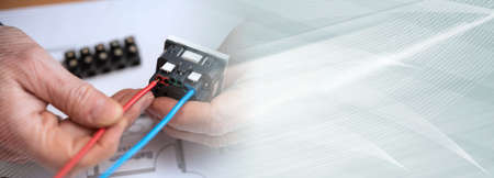 Electrician hands connecting a wire into a power socket; panoramic banner