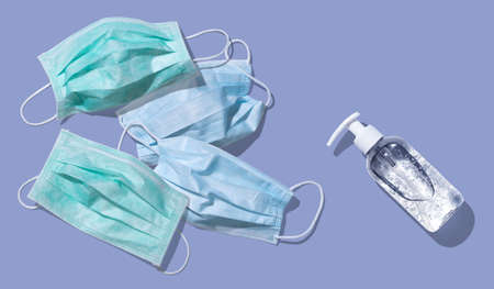 Face masks and sanitizer bottle dispenser for virus preventive measure on light violet background; top viewの写真素材