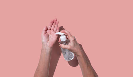 Hands using sanitizer bottle dispenser for coronavirus preventive measure on light coral color...