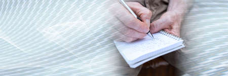 Man taking notes on a pocket book, closeup; panoramic banner