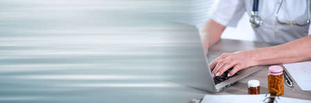 Female doctor using laptop in medical office; panoramic banner