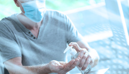 Man using hand sanitizer alcohol gel; prevention of virus and bacteria infection; light effectの写真素材
