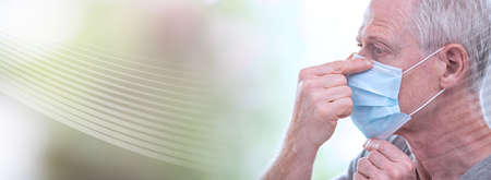 Portrait of senior man putting on a medical mask on his face; panoramic bannerの写真素材