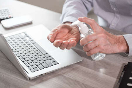 Businessman applying sanitizer on his hands before using laptop; concept of prevention and protection against virus infectionの写真素材