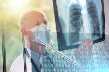 Doctor wearing a medical face mask and examining lungs x-ray during coronavirus outbreak; multiple exposureの写真素材