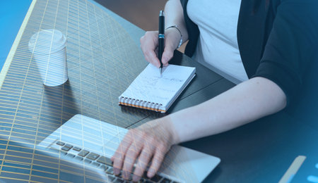 Businesswoman taking notes while using laptop; multiple exposure
