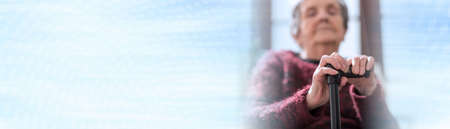 Old woman sitting with her hands on a cane; panoramic bannerの写真素材