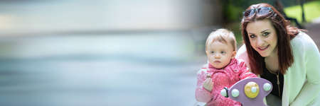 Portrait of happy young mother with her baby girl in a playground, outside; panoramic bannerの写真素材