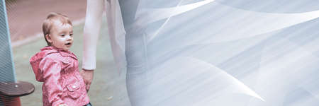 Mother holding her baby girl by hand and walking on playground; panoramic bannerの写真素材
