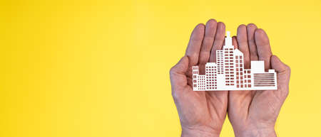 Concept of business insurance with paper building in hands on yellow backgroundの写真素材
