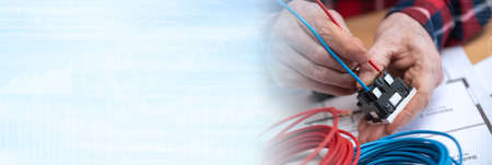 Electrician hands connecting a wire into a power socket; panoramic banner