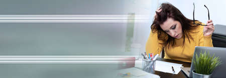 Desperate young businesswoman with hand on head sitting at desk; panoramic banner