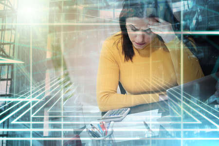 Desperate young businesswoman with hand on forehead sitting at desk; multiple exposureの写真素材