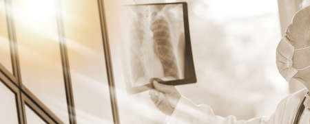 Doctor wearing a medical face mask and examining lungs x-ray during virus outbreak; multiple...