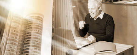 smiling senior businessman showing success gesture in front of his laptop; multiple exposureの写真素材
