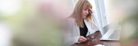 Stressed businesswoman sitting in office with hand on forehead; panoramic bannerの写真素材