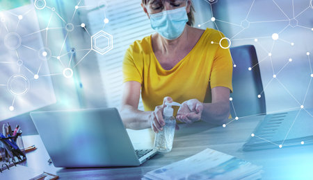 Businesswoman wearing a medical face mask and applying sanitizer on her hands; light-effectの写真素材
