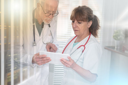 Two mature doctors discussing about medical report on digital tablet; multiple exposureの写真素材