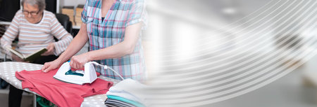 Home helper ironing clothes for elderly woman; panoramic bannerの写真素材