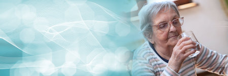 Elderly woman holding a glass of water at home; panoramic bannerの写真素材