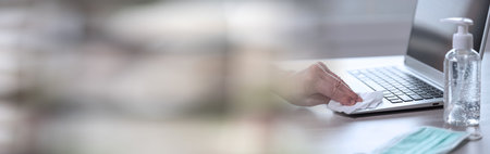 woman disinfecting laptop keyboard with antibacterial wipe; prevention of virus and bacteria infection; panoramic bannerの写真素材