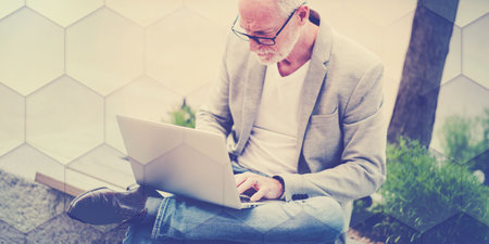 Mature businessman sitting on a bench outdoors and using laptop, geometric patternの写真素材