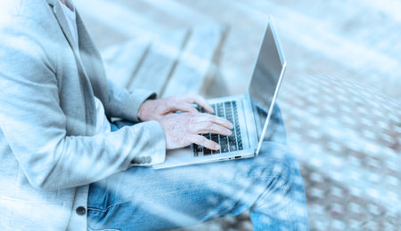 Businessman sitting on a bench outdoors and using laptop; light-effect