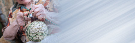 Senior woman knitting at home; panoramic banner