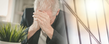 Overworked and exhausted senior businessman sitting at workplace; multiple exposureの写真素材