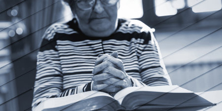 Elderly woman praying with her hands over the bible, geometric patternの写真素材