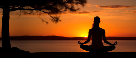 Silhouette of young woman practicing yoga outdoors on the beach at sunsetの素材