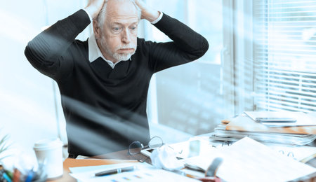 Overworked businessman sitting at a messy desk in office; light effect