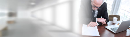 Senior businessman reading and checking document in office (lorem ipsum text used); panoramic banner