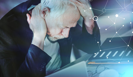 Overworked and exhausted senior businessman sitting at workplace; light effect