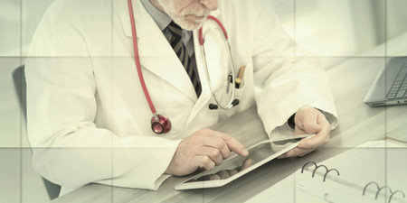 Male senior doctor using digital tablet in medical office, geometric patternの写真素材