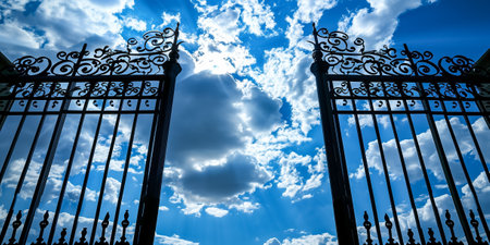 Detailed view of ornate wrought iron gates set against a bright sky with clouds and sunlightの素材