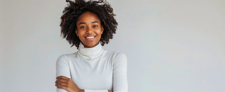Confident young woman with curly hair, smiling in a white turtleneck against a plain backgroundの素材