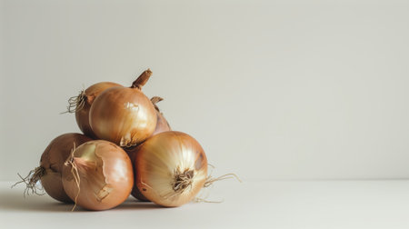 Stack of fresh brown onions with roots on a light, neutral backgroundの素材