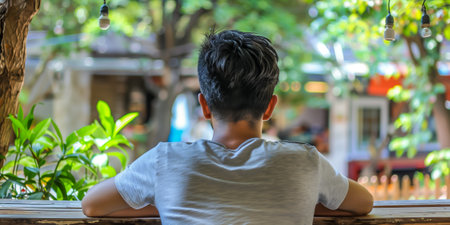 A young person is seated outdoors, reflecting while observing a serene cafÃ©の素材