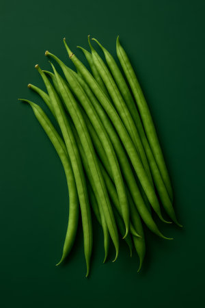 A visually appealing arrangement of fresh green beans on a dark green surfaceの素材