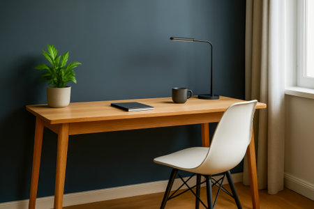 A stylish workspace featuring a wooden desk, lamp, plant, and notebook against a dark wallの素材