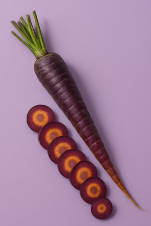 A whole purple carrot with slices arranged on a purple background for a vibrant lookの素材