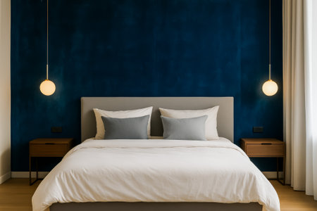 A modern bedroom featuring a blue accent wall, stylish bed, and elegant lightingの素材