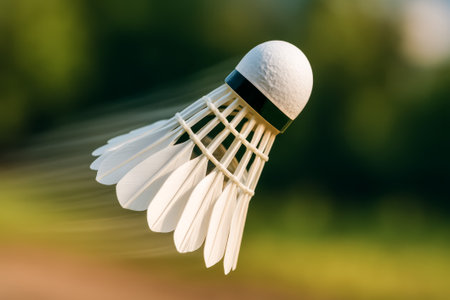 A badminton shuttlecock captured in motion, showing its feathers and form against greeneryの素材