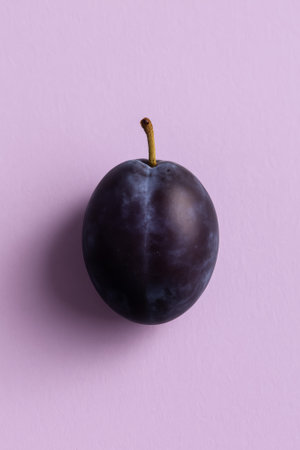 A fresh purple plum placed on a soft pink background for aesthetic appealの素材