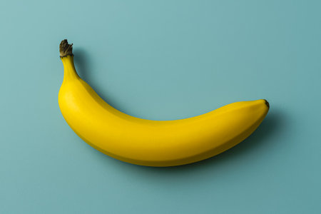 A single ripe banana laid out on a smooth light blue backgroundの素材