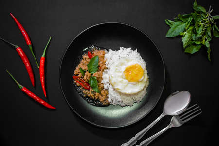 Rice with pork stir fried with basil and fried egg on black background, Thai food, Street food,...