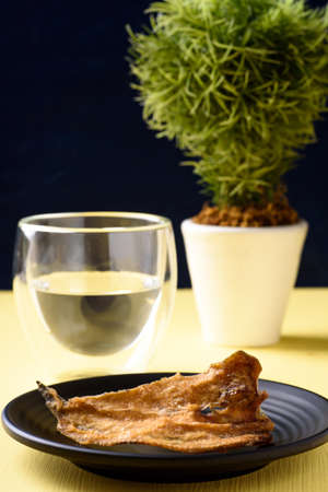 Fried dry fish on black dish and glass of water, Asian cuisine
